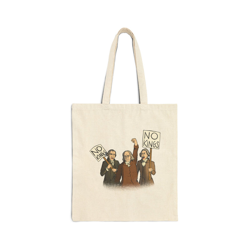 An off-white canvas tote bag with two straps and a graphic on a plain white background. The bag has a printed illustration of three Disappointed American Founders protesting and holding 'NO KINGS' signs.