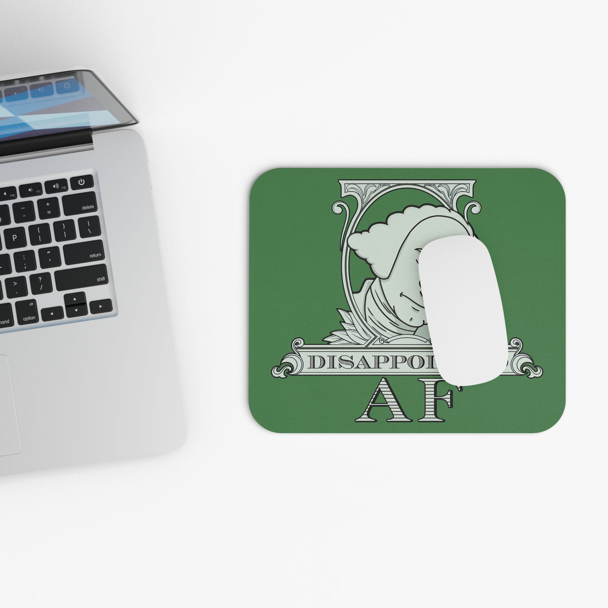 A square green mousepad with a mouse on top of it, all on a white background with rounded corners featuring a logo in the center. This is the logo for Disappointed AF and is framed with scrolls, similar to that of a dollar bill, with George Washington in the center. George Washington looks disappointed, is leaning his head forward, and has his head in his hand with an exasperated look on his face. Below the figure it says Disappointed AF. A laptop computer is partially in view on the left side of the frame